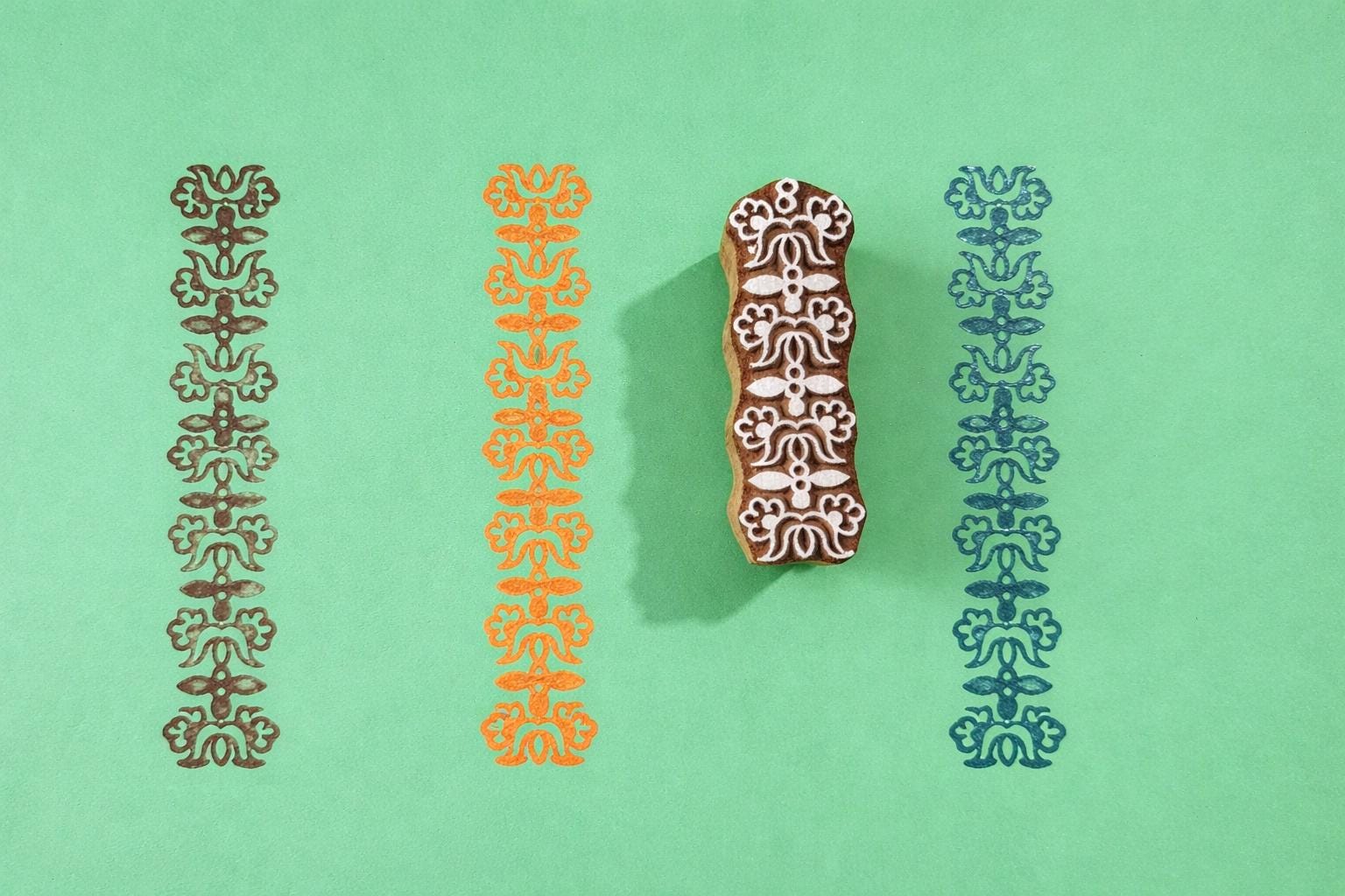 Hand carved wooden heritage motif border block printing stamp creating repeating vertical pattern on green background.