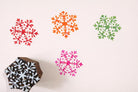 Hand carved wooden floral snowflake block printing stamp creating colorful snowflake prints on white paper.