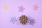 Hand carved wooden arrow snowflake block printing stamp creating colorful geometric snowflake prints on pastel background.