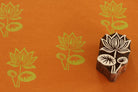 Hand carved Indian wooden printing block with a detailed lotus flower design shown on orange paper with repeated lotus prints.