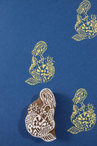 Hand carved wooden mermaid block printing stamp creating yellow ink impressions on blue paper.