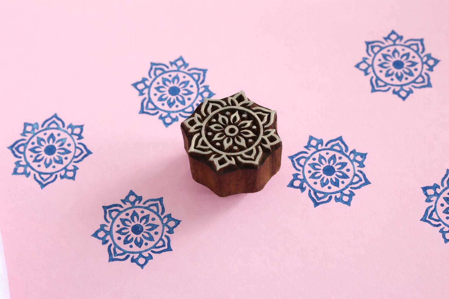 Hand carved mandala flower wooden block stamp on pink background with blue floral repeat prints.