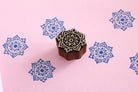 Hand carved mandala flower wooden block stamp on pink background with blue floral repeat prints.