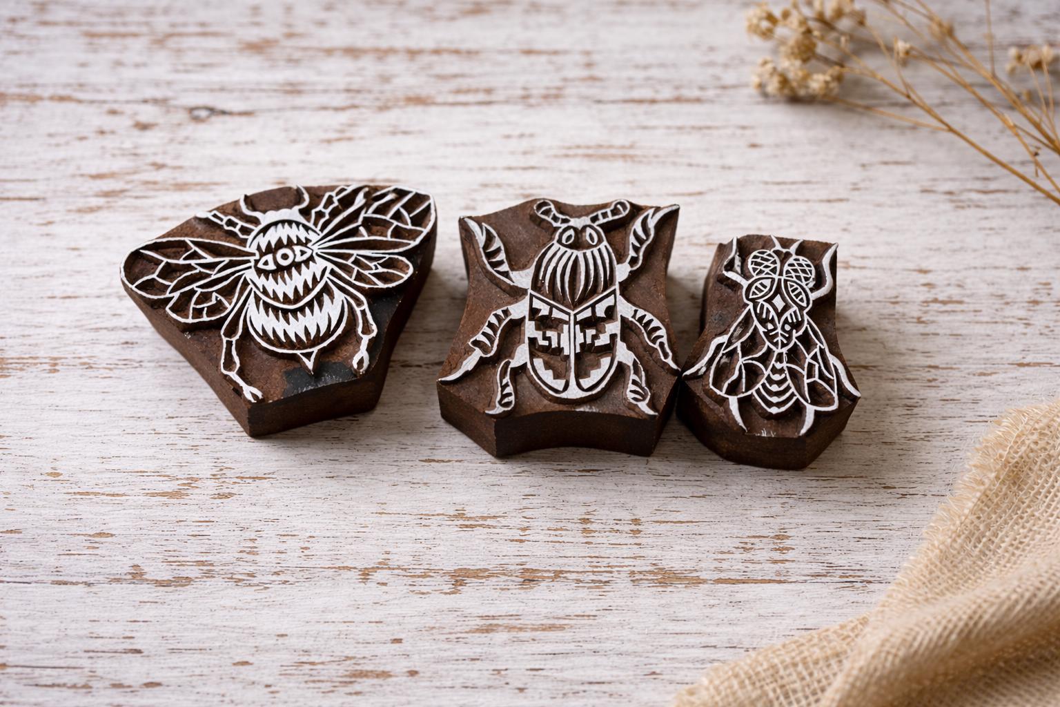 Set of three hand carved wooden insect block printing stamps featuring bee, beetle and fly designs on rustic white background.