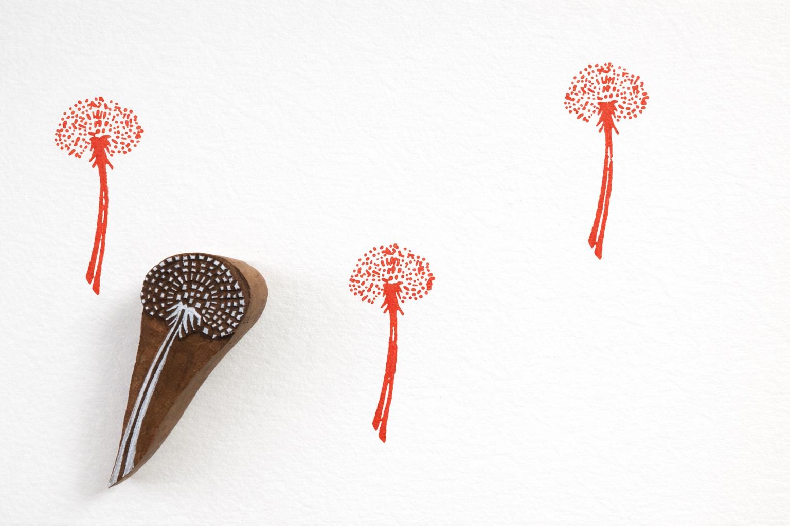 Hand carved wooden dotted seed head block printing stamp creating red botanical prints on white paper.