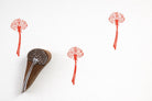 Hand carved wooden dotted seed head block printing stamp creating red botanical prints on white paper.