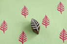 Hand carved wooden fern leaf printing block shown with pink fern prints on light green paper.