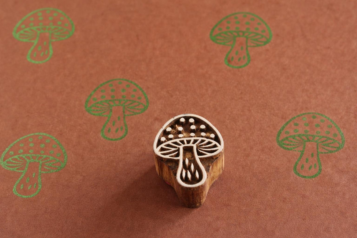 Hand carved wooden mushroom printing block shown with green mushroom prints on brown paper.