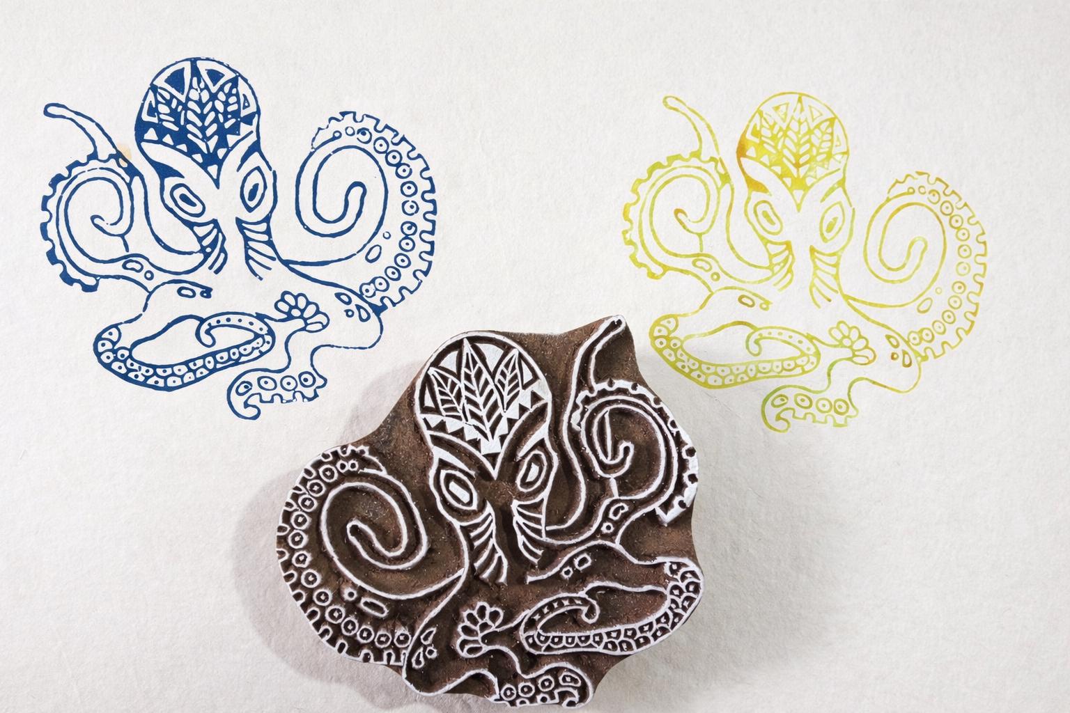 Hand carved wooden octopus block printing stamp with detailed tentacles shown with blue and yellow ink impressions.