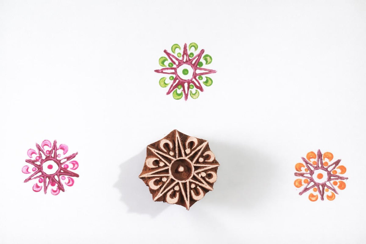 Hand carved wooden eight point star block printing stamp with colorful star impressions on white background.