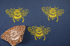 Hand carved wooden bumblebee block printing stamp creating yellow bee prints on dark blue paper.