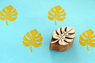 Hand carved monstera leaf wooden stamp with yellow printed pattern on blue background.