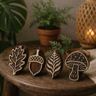 Set of four hand carved wooden printing blocks featuring oak leaf, acorn, fern leaf and mushroom designs displayed on rustic wooden table.