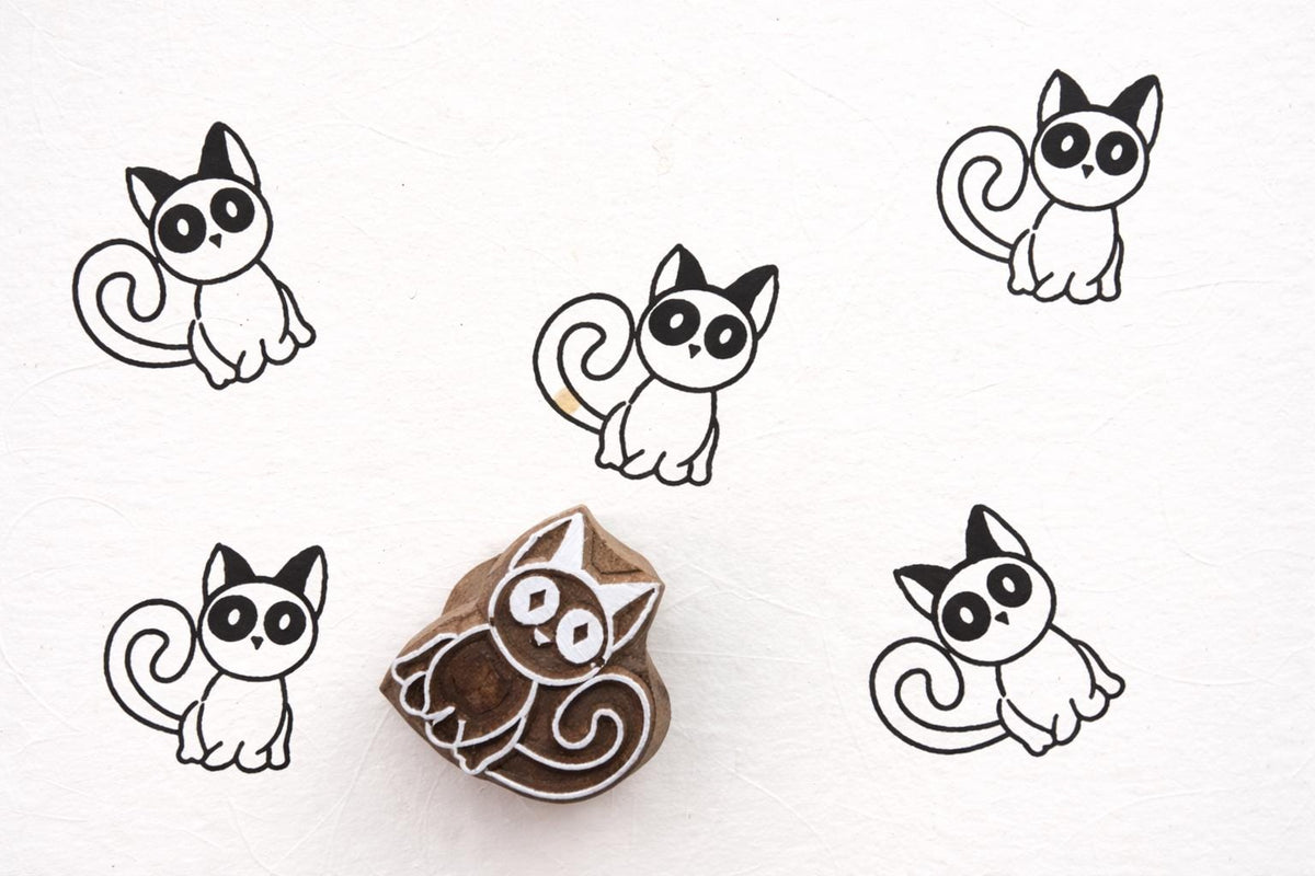 Hand carved wooden kitten block printing stamp creating black cat prints on white paper.