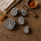 Set of five hand carved wooden paisley block printing stamps displayed on rustic wooden table with natural fabric and spice bowl.