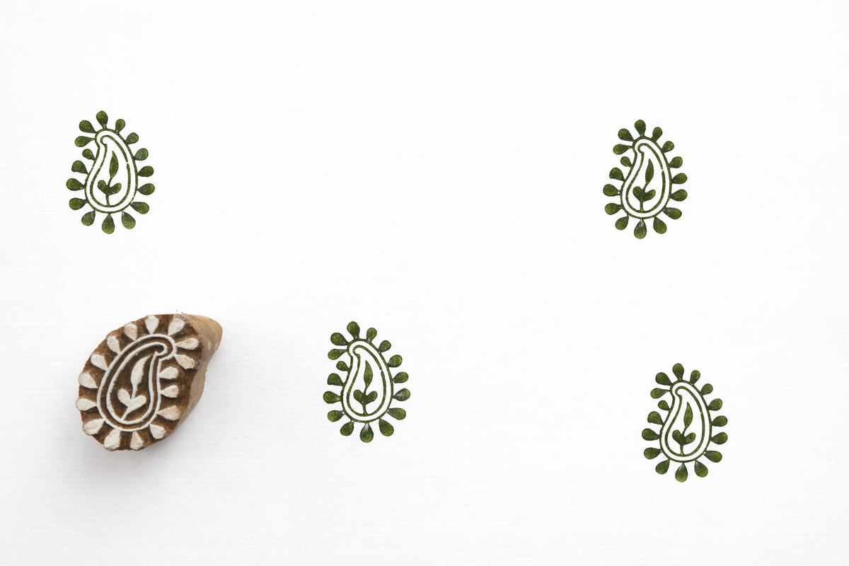 Hand carved decorative paisley wood block stamp creating green repeat prints on white paper.