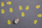 Small hand carved paisley wood block stamp creating yellow repeat prints on dark paper.