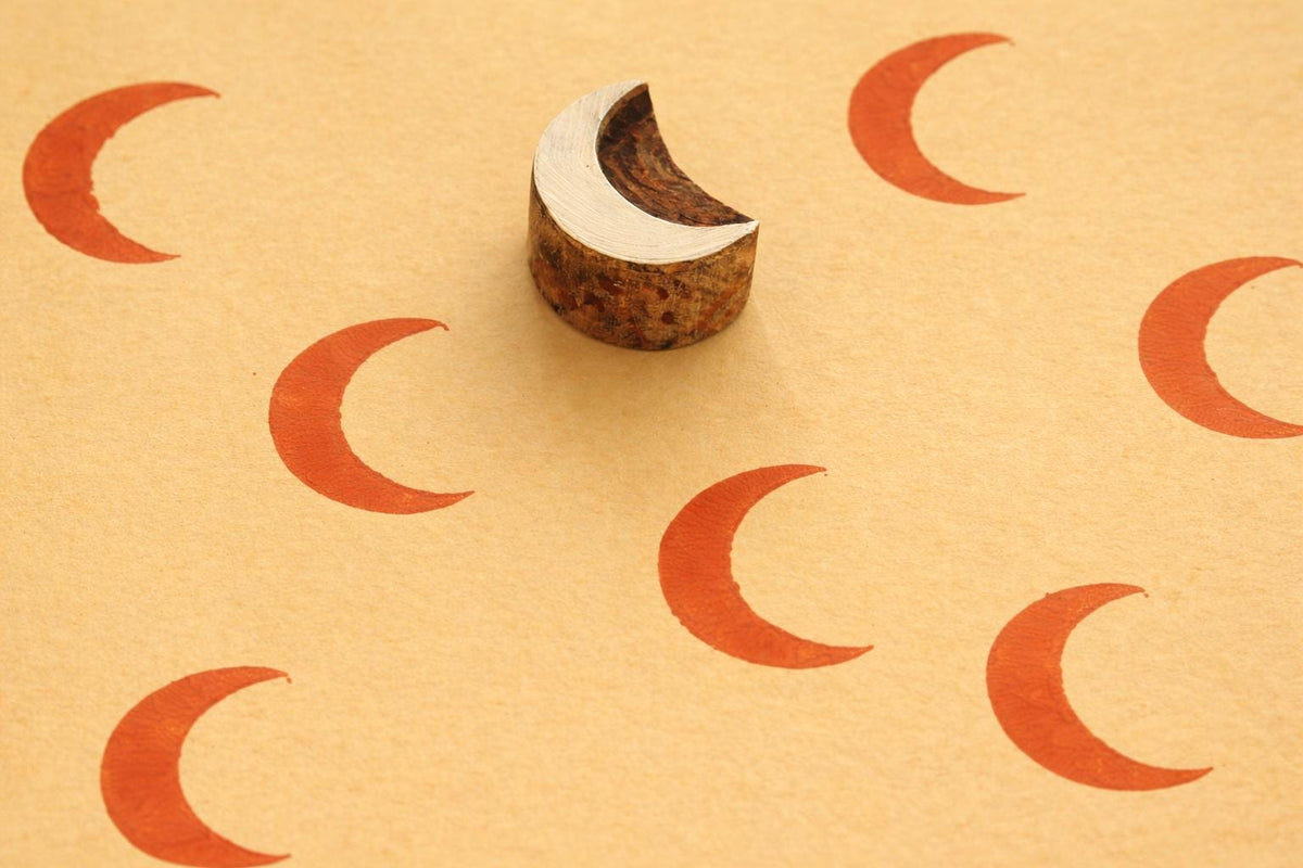 Hand carved wooden crescent moon block stamp making orange prints on handmade paper