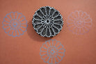 Hand carved round wooden mandala block printing stamp creating blue and purple radial floral pattern on orange background.