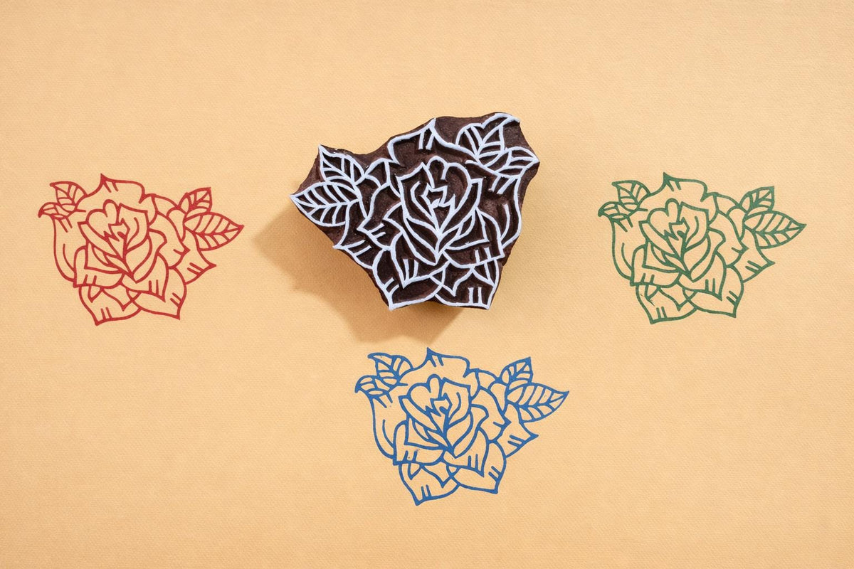Hand carved wooden rose block printing stamp creating red, green and blue rose prints on yellow paper.