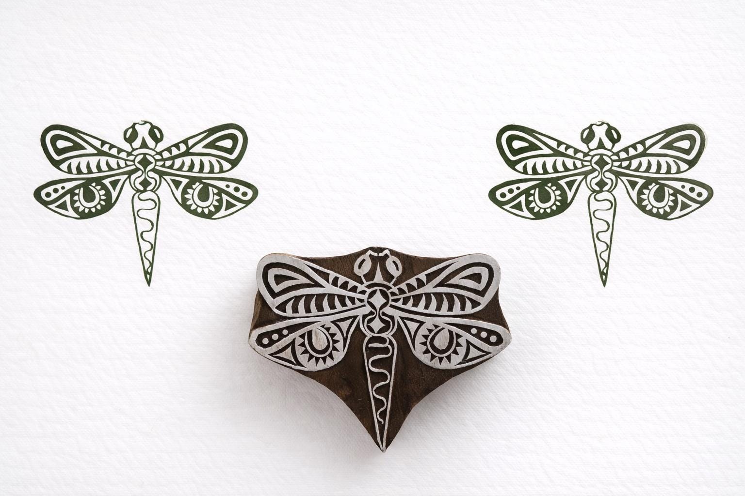 Hand carved wooden dragonfly block printing stamp creating green dragonfly prints on white paper background.