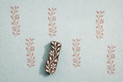 Indian wooden vine block printing stamp with small flowers creating repeating botanical pattern on blue background.