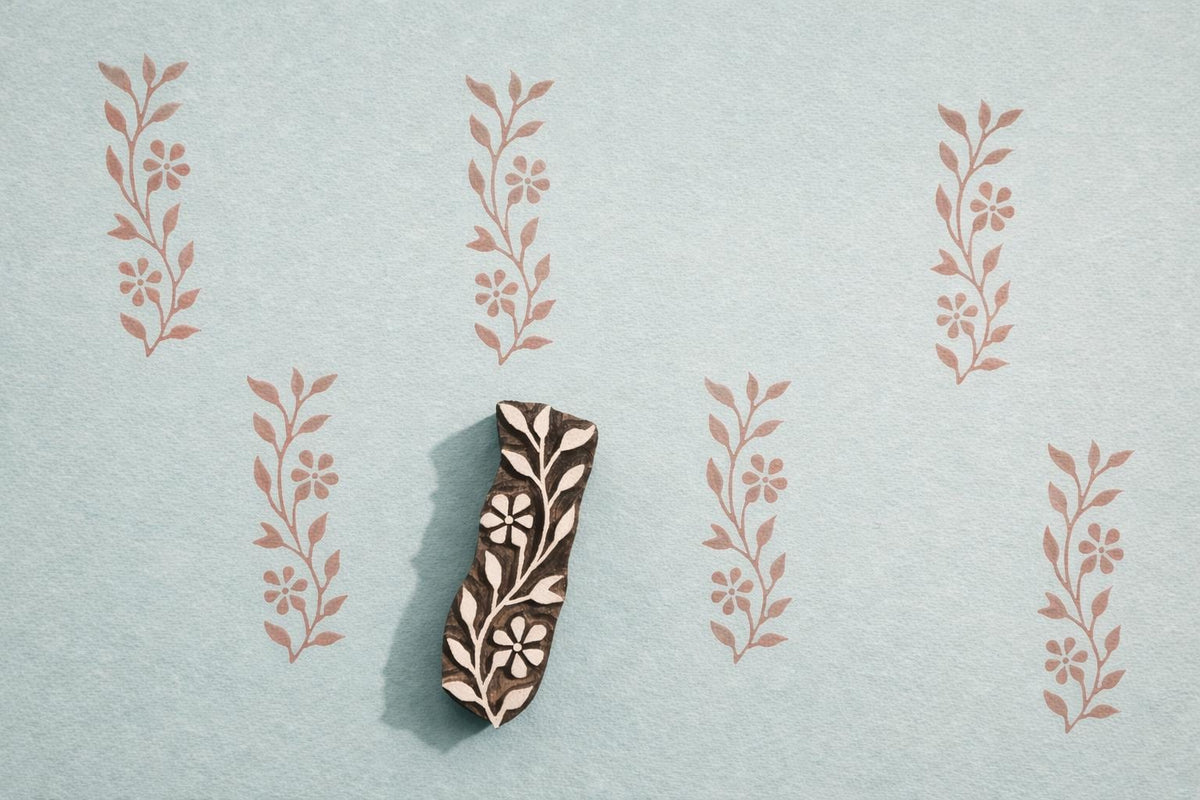 Indian wooden vine block printing stamp with small flowers creating repeating botanical pattern on blue background.