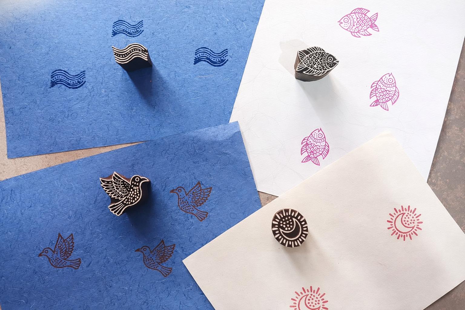 Hand carved wooden block printing stamps creating bird, fish, moon and wave prints on colored handmade paper.