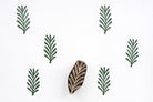 Hand carved wooden fern leaf block printing stamp creating repeating green botanical pattern on white background.