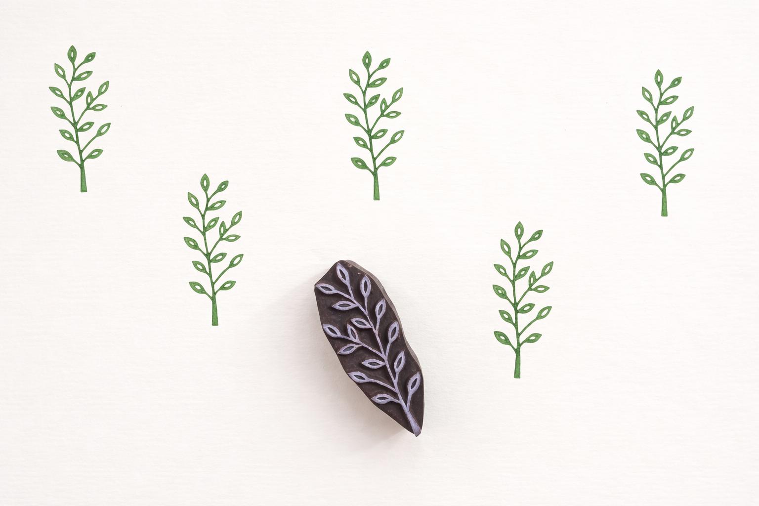 Slim branch leaf wooden block printing stamp creating repeating green vine pattern on cream background.