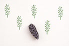 Slim branch leaf wooden block printing stamp creating repeating green vine pattern on cream background.