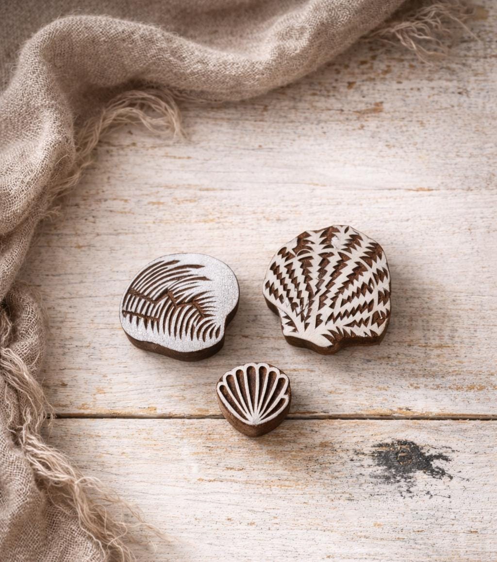 Hand carved wooden block printing stamps featuring seashell designs arranged on a off white background with a linen scarf as a prop
