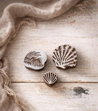 Hand carved wooden block printing stamps featuring seashell designs arranged on a off white background with a linen scarf as a prop