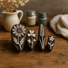 Set of four hand carved wooden floral block printing stamps displayed on rustic wooden table with ceramic vase and linen cloth.