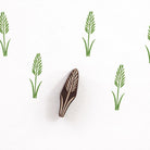 Tall wheat style wooden block printing stamp creating repeating green botanical pattern on white background.