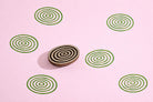 Oval wooden block printing stamp with concentric circle design creating repeating green ripple pattern on pink background.
