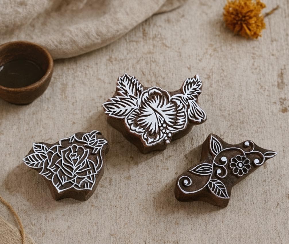 Set of three hand carved wooden floral block printing stamps featuring rose, hibiscus and vine design on neutral fabric background.