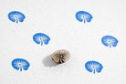Small teardrop shaped lily pad wooden printing stamp making repeating blue leaf pattern on white background.