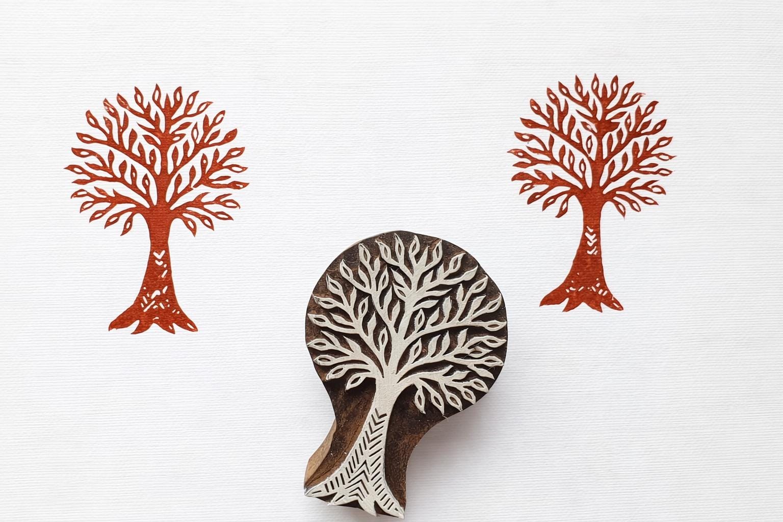 Hand carved wooden tree block printing stamp with two printed tree designs on white paper.