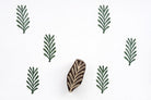 Hand carved wooden fern leaf block printing stamp creating repeating green botanical pattern on white background.