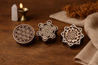 Hand carved wooden sacred geometry block printing stamps featuring flower of life, metatron cube, and sri yantra designs on a wooden table.