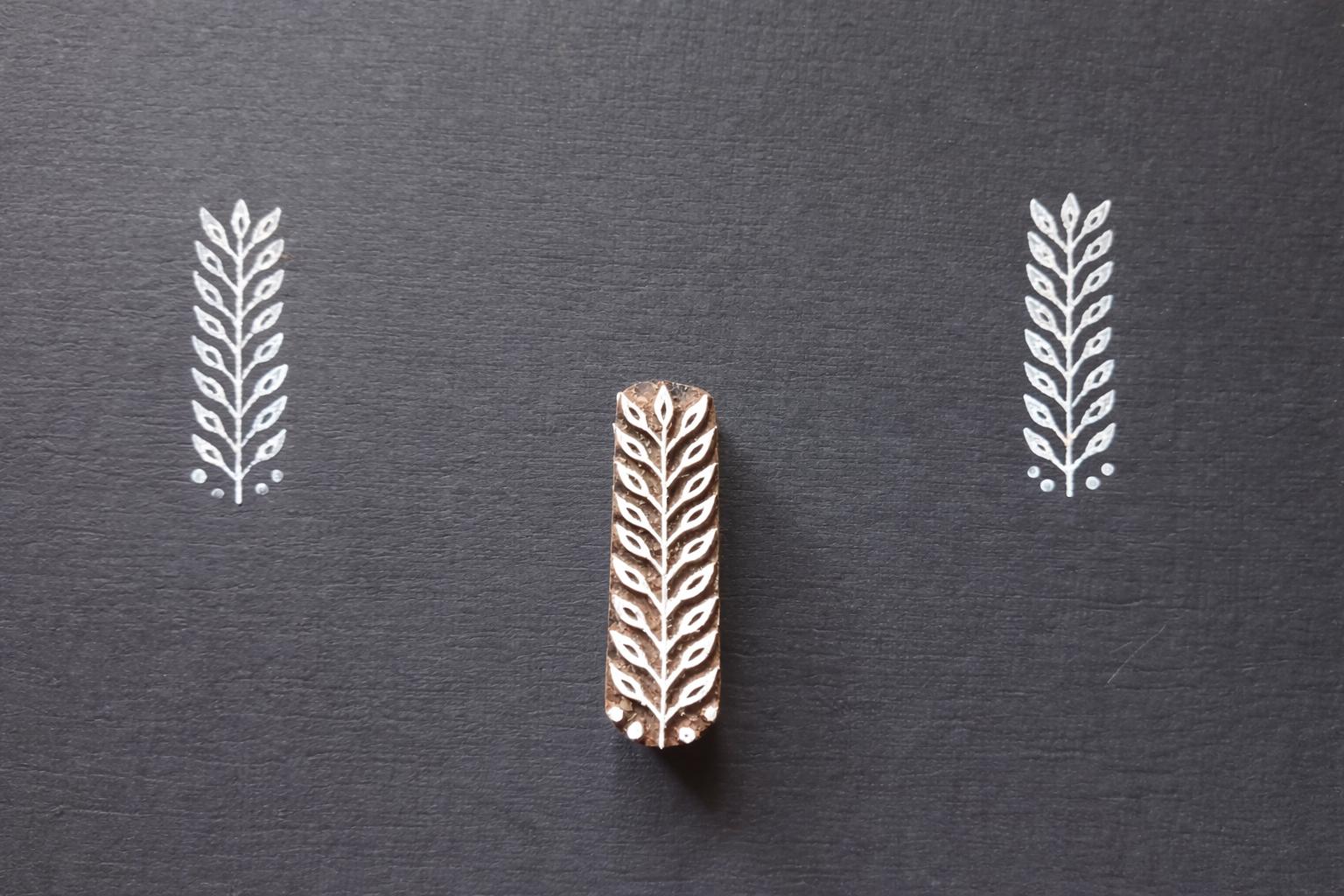 Hand carved leaf textile stamp made from wood showing white leaf prints on dark paper.