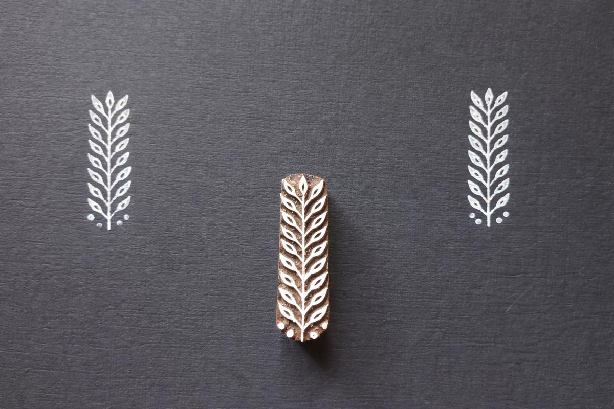 Hand carved leaf textile stamp made from wood showing white leaf prints on dark paper.