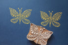 Butterfly block printing stamp made from carved wood with yellow butterfly prints on blue paper.