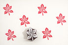 Hand carved four-leaf wooden block printing stamp creating repeating red botanical motif pattern on cream fabric.