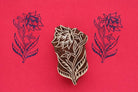 Hand carved wooden block printing stamp featuring large layered botanical flower with flowing leaves creating dark blue print on red background.