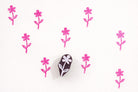 Small hand carved wooden flower block printing stamp creating repeating pink floral pattern on white background.