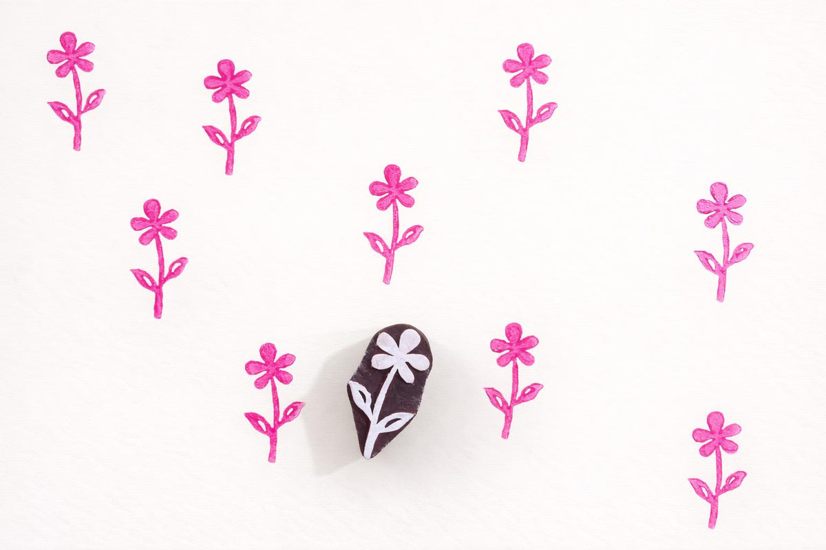 Small hand carved wooden flower block printing stamp creating repeating pink floral pattern on white background.