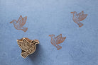 Hand carved wooden bird block printing stamp creating brown bird prints on blue handmade paper.