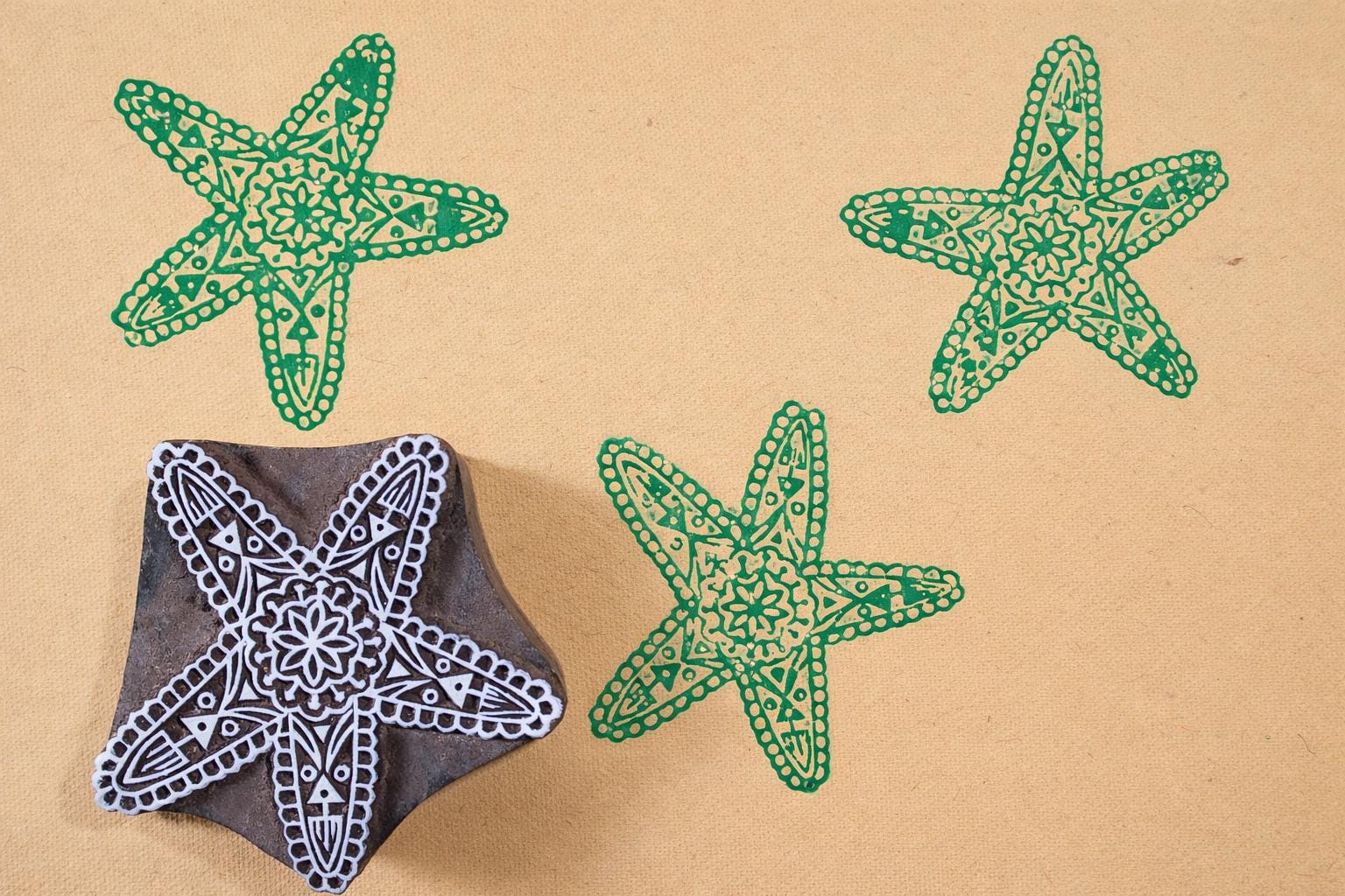Hand carved wooden starfish block printing stamp creating green ink prints on yellow fabric.
